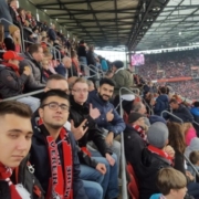 Jugendliche mit Fanschals des 1. FC Kölns sitzen im Stadion auf einer vollen Tribüne